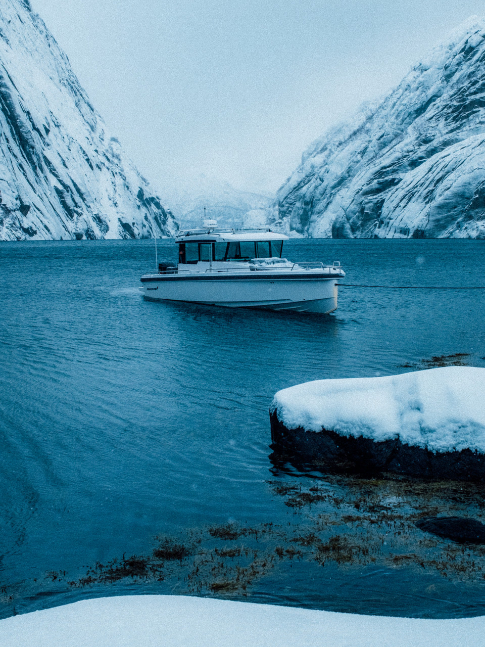 L’Axopar 37 au mouillage dans un fjord des Lofoten, entre des parois de roche enneigée